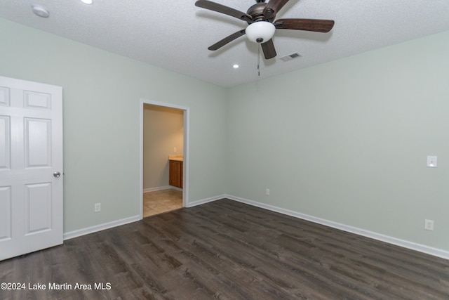 unfurnished bedroom with a textured ceiling, ceiling fan, ensuite bathroom, and dark wood-type flooring