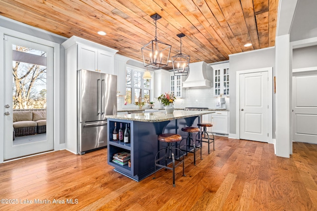 kitchen featuring appliances with stainless steel finishes, wood ceiling, custom exhaust hood, white cabinets, and a kitchen island