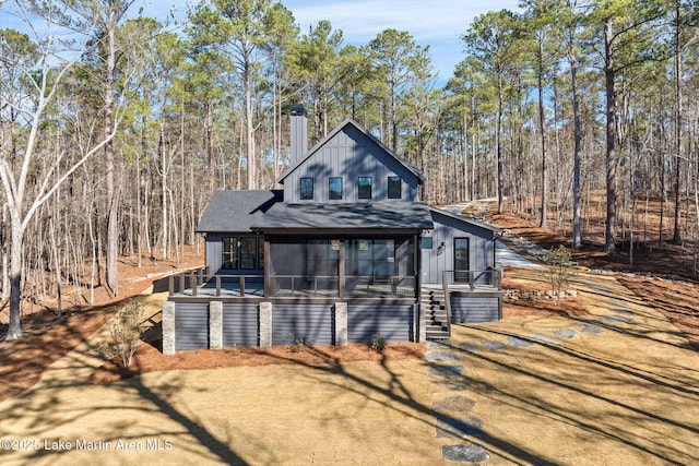 back of property with roof with shingles, stairs, a chimney, and a wooded view