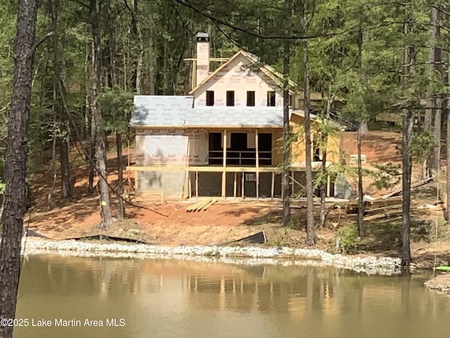 back of house featuring a wooded view, a water view, and a chimney