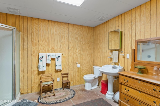 bathroom with tile patterned flooring, toilet, a shower with shower door, and wooden walls