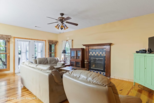 living room featuring a fireplace, ceiling fan, french doors, and light wood-type flooring