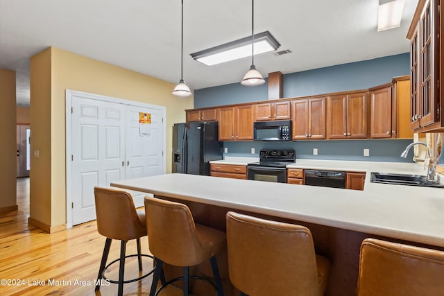 kitchen with sink, black appliances, decorative light fixtures, light hardwood / wood-style floors, and a breakfast bar area