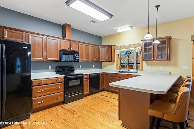 kitchen with kitchen peninsula, a kitchen bar, black appliances, light hardwood / wood-style floors, and hanging light fixtures