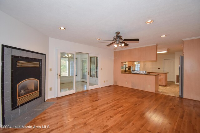 unfurnished living room with a tile fireplace, light hardwood / wood-style floors, ceiling fan, and sink