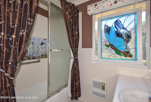 bathroom with heating unit, sink, tile walls, and combined bath / shower with glass door