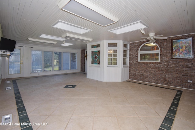 unfurnished room with ceiling fan, light tile patterned floors, brick wall, and a skylight