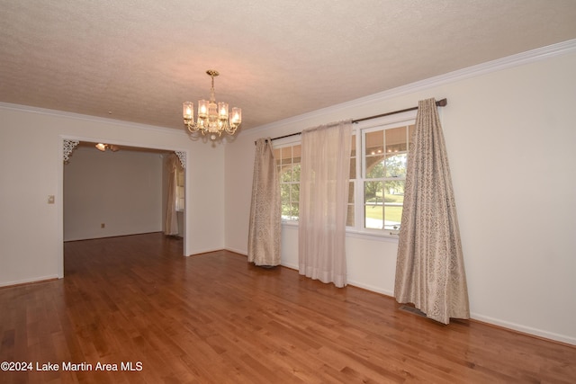 empty room featuring a notable chandelier, wood-type flooring, a textured ceiling, and ornamental molding