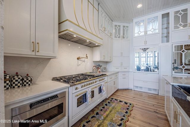 1071 Trillium W Pkwy, Eclectic, AL 36024 - kitchen with white cabinets, built in microwave, range with two ovens, light wood-type flooring, and custom exhaust hood