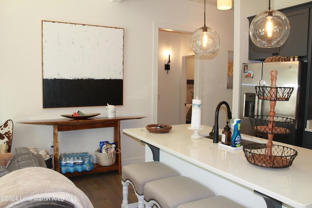 kitchen featuring stainless steel fridge, kitchen peninsula, hanging light fixtures, and dark wood-type flooring