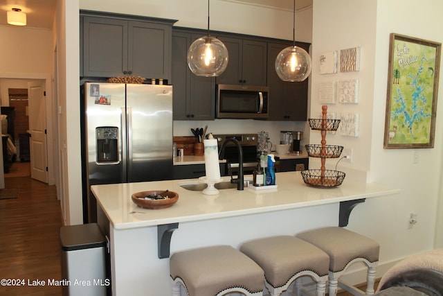 kitchen with dark wood-type flooring, pendant lighting, stainless steel appliances, and a kitchen breakfast bar