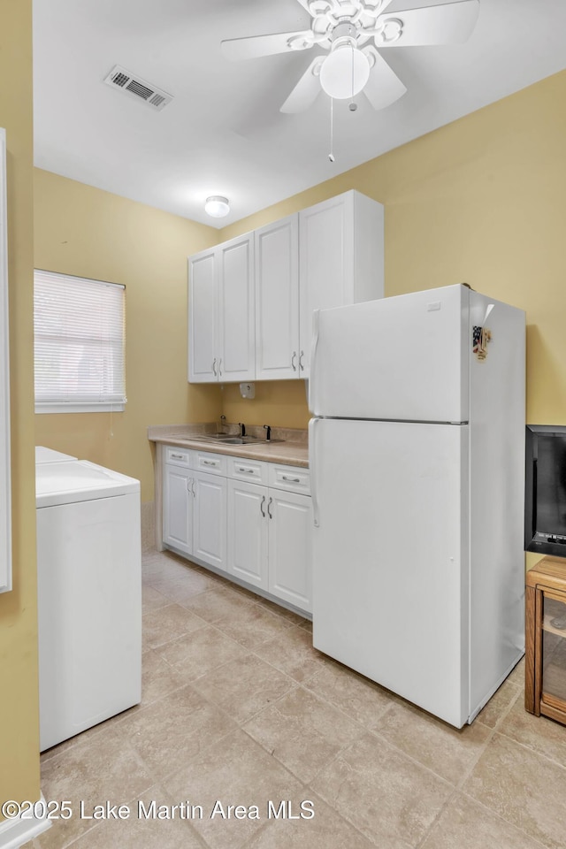 kitchen with visible vents, freestanding refrigerator, washer / clothes dryer, white cabinetry, and a ceiling fan