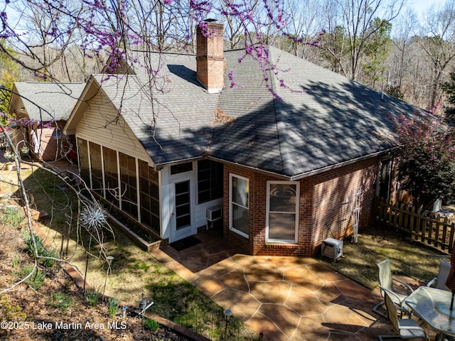 rear view of property featuring a patio, a shingled roof, a sunroom, brick siding, and a chimney