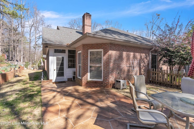 rear view of house with brick siding, a shingled roof, fence, a chimney, and a patio area