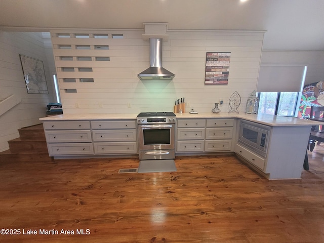 kitchen featuring wall chimney range hood, kitchen peninsula, gray cabinetry, stainless steel appliances, and dark hardwood / wood-style flooring