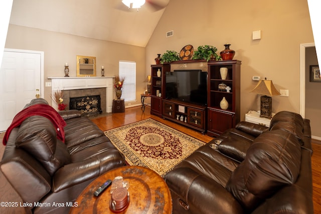 living room with hardwood / wood-style flooring, a tiled fireplace, and high vaulted ceiling