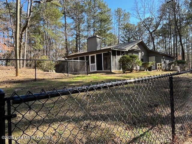 view of side of home with a sunroom, a fenced backyard, and a chimney