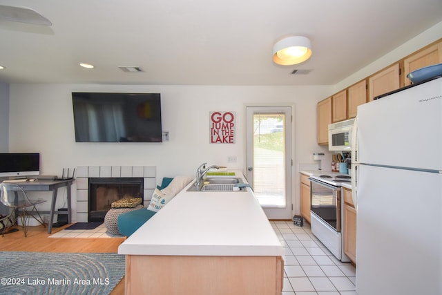 kitchen featuring white appliances, sink, light brown cabinetry, a kitchen island, and a tiled fireplace