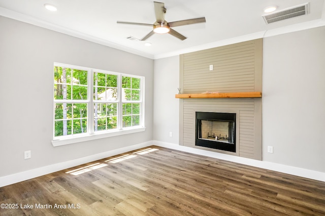 unfurnished living room featuring a ceiling fan, a large fireplace, wood finished floors, baseboards, and crown molding
