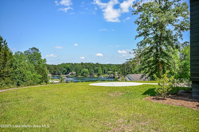 view of grassy yard with a water view and a forest view