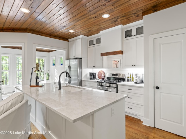 kitchen featuring light stone counters, white cabinetry, stainless steel appliances, and an island with sink