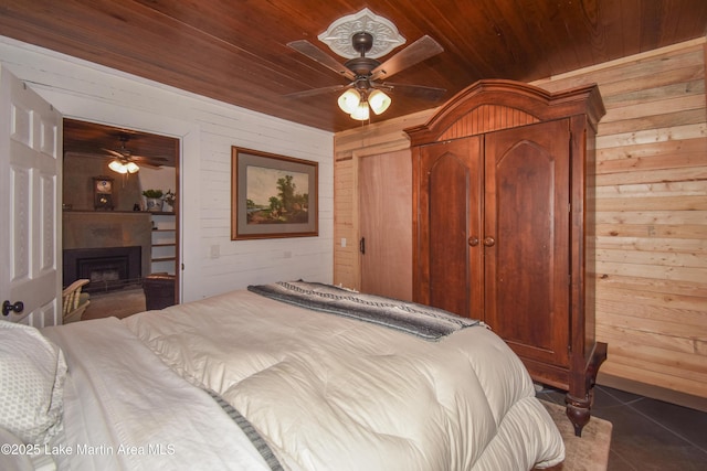 bedroom featuring wood ceiling, a fireplace, dark tile patterned floors, and wood walls