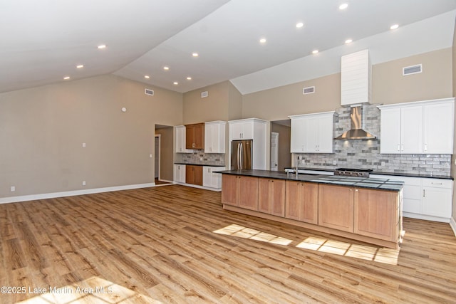 kitchen with a large island with sink, white cabinets, wall chimney exhaust hood, tasteful backsplash, and stainless steel refrigerator