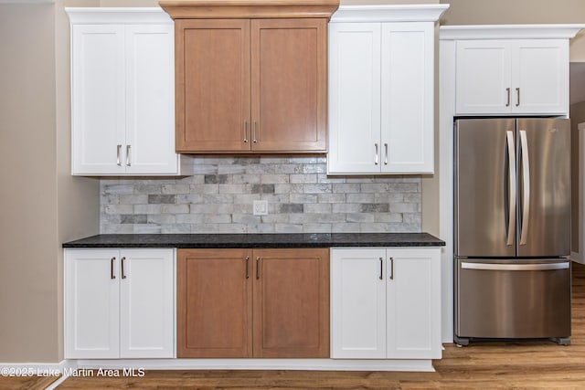 kitchen featuring stainless steel fridge, tasteful backsplash, white cabinetry, and dark stone countertops