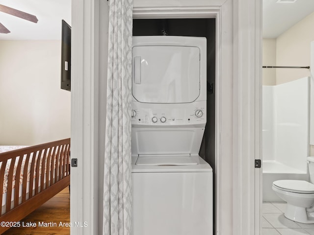 clothes washing area with visible vents, a ceiling fan, stacked washing maching and dryer, laundry area, and tile patterned floors