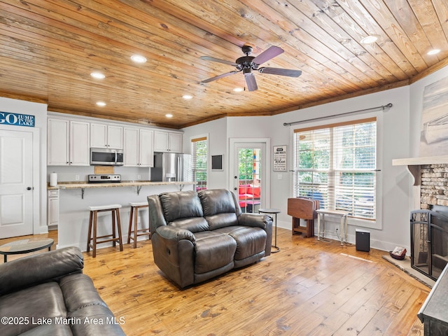 living room with light wood-style floors, wood ceiling, crown molding, and a stone fireplace