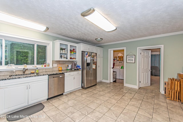 kitchen featuring appliances with stainless steel finishes, dark stone countertops, sink, washing machine and clothes dryer, and white cabinets