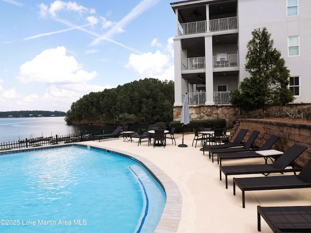 community pool featuring a patio area, a water view, and fence