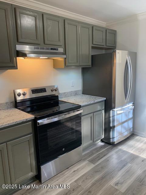 kitchen with light wood-type flooring, appliances with stainless steel finishes, ornamental molding, and light stone countertops