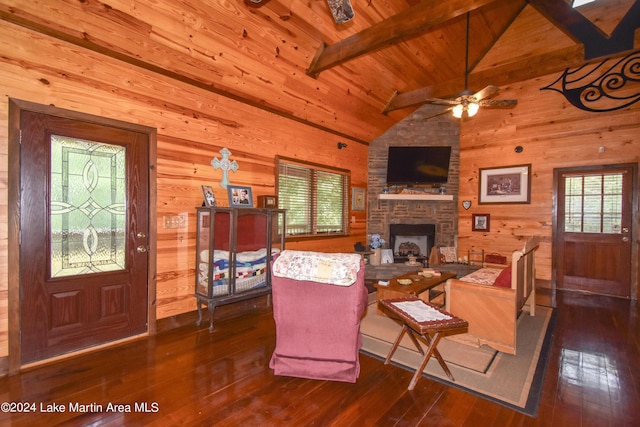 living room with ceiling fan, dark wood-type flooring, vaulted ceiling with beams, a stone fireplace, and wood walls