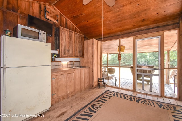 kitchen with light wood-type flooring, vaulted ceiling, wooden walls, sink, and white fridge