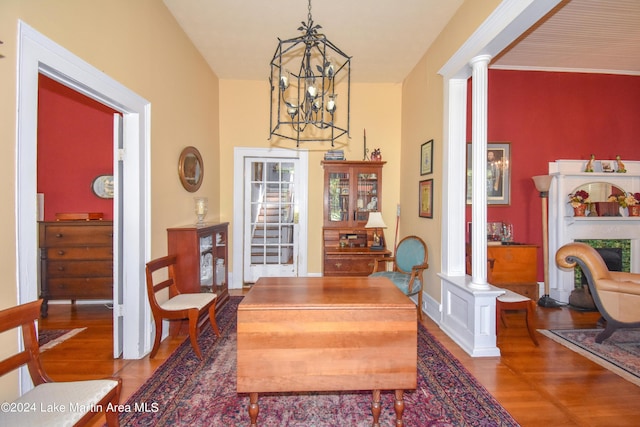 dining space with a fireplace, wood-type flooring, an inviting chandelier, and ornate columns