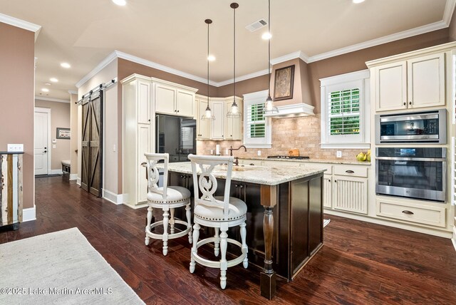 3408 Quail Cv, Opelika, AL 36801 - kitchen with stainless steel appliances, a barn door, crown molding, backsplash, and light stone countertops