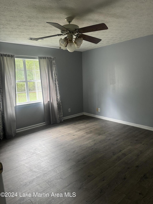 spare room with a textured ceiling, dark wood-type flooring, a ceiling fan, and baseboards