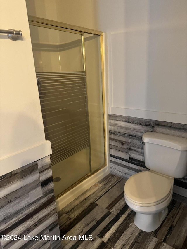 full bath featuring a shower stall, toilet, and wood finished floors