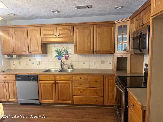 kitchen featuring visible vents, dark wood-style floors, glass insert cabinets, appliances with stainless steel finishes, and a sink