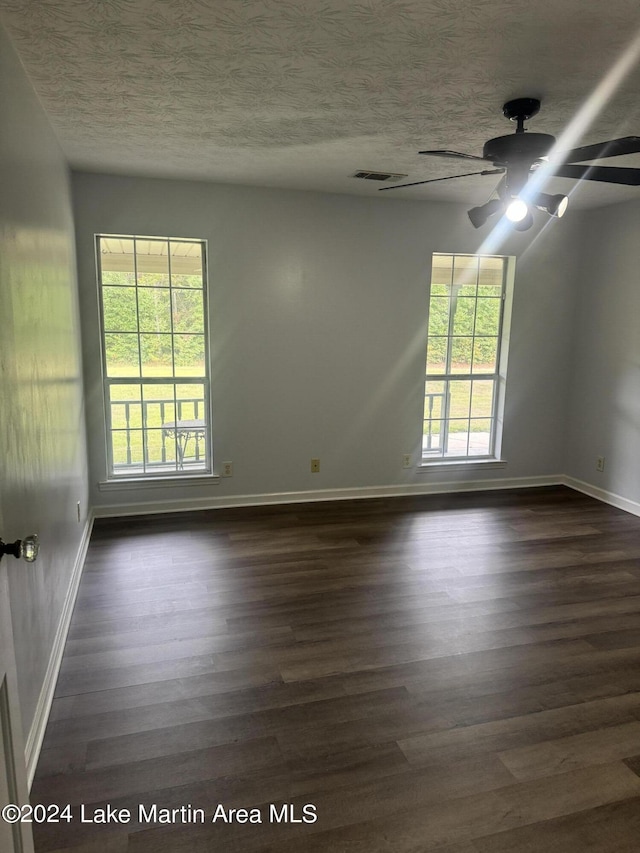 spare room featuring plenty of natural light, a textured ceiling, visible vents, and dark wood-style flooring