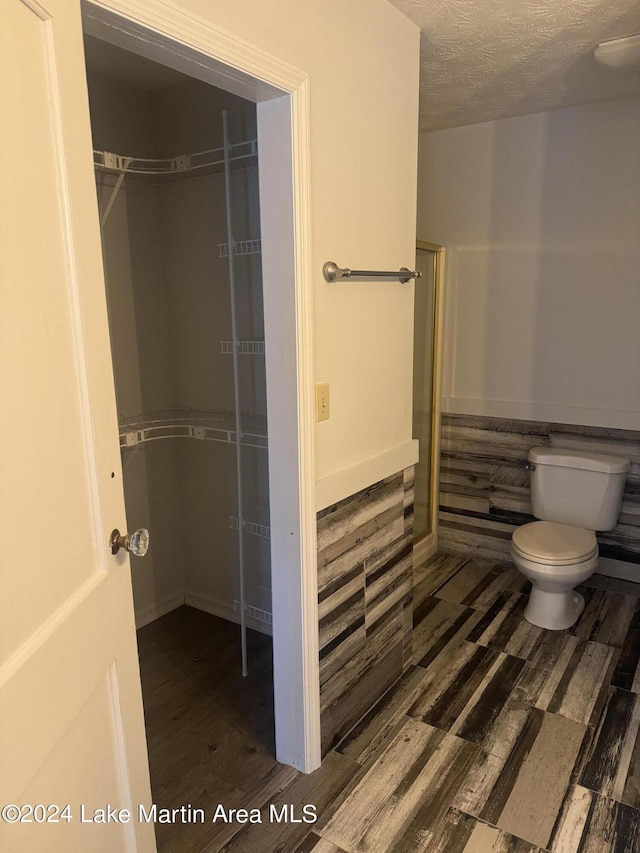 full bathroom with toilet, a textured ceiling, walk in shower, and wood finished floors