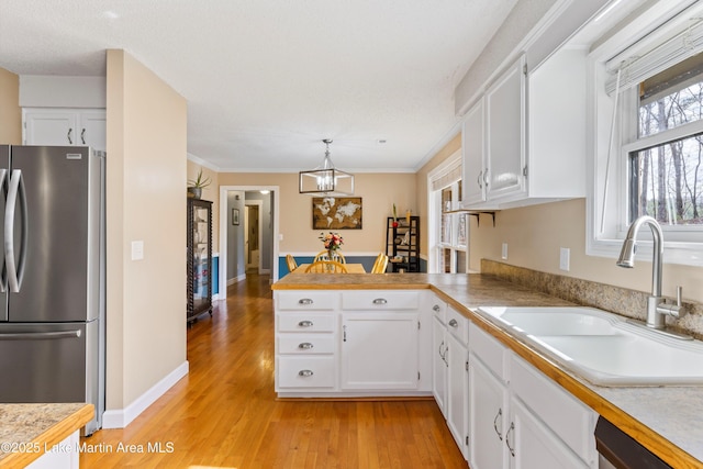 kitchen with a peninsula, a sink, white cabinets, freestanding refrigerator, and decorative light fixtures