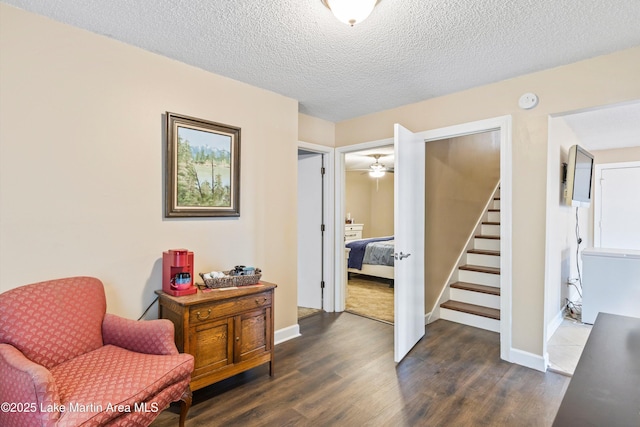 living area featuring dark wood-type flooring, a textured ceiling, baseboards, and stairs