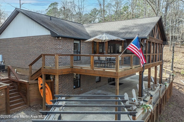 rear view of house featuring stairs, a shingled roof, brick siding, and a deck