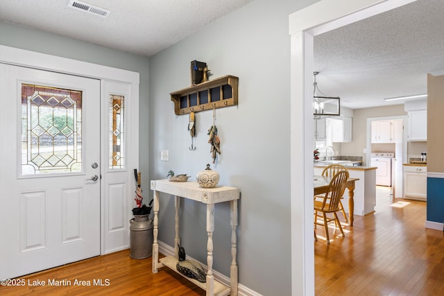 entryway with a textured ceiling, washer and dryer, light wood-style flooring, baseboards, and visible vents
