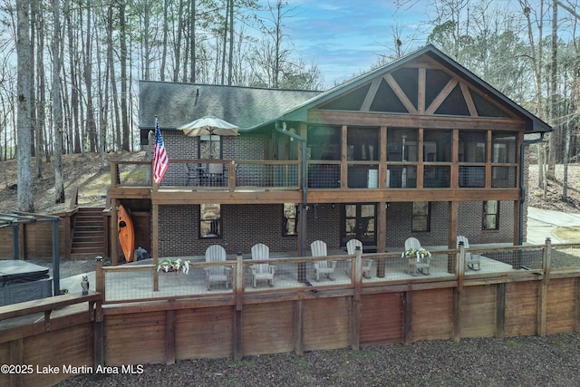 view of front of home featuring a deck, brick siding, a sunroom, stairway, and roof with shingles