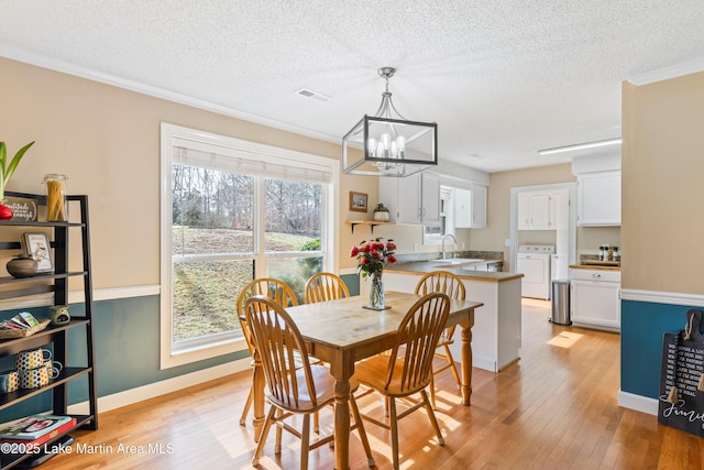 dining room featuring a notable chandelier, separate washer and dryer, visible vents, light wood-style floors, and ornamental molding