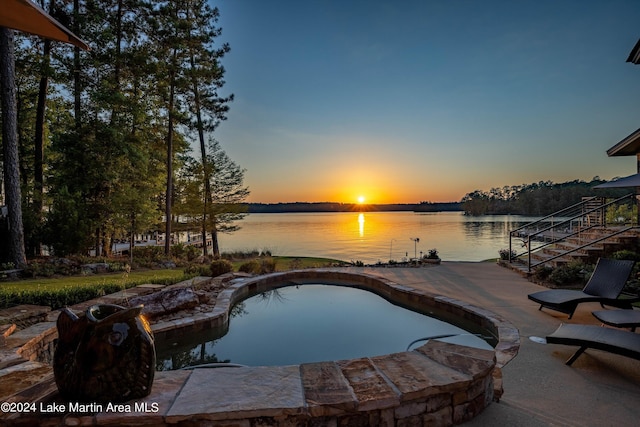 pool at dusk with a patio and a water view