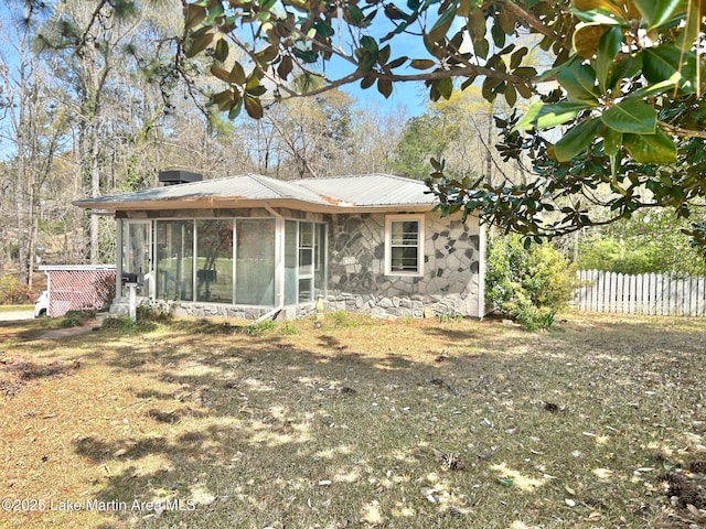 rear view of property with stone siding, a sunroom, fence, and metal roof
